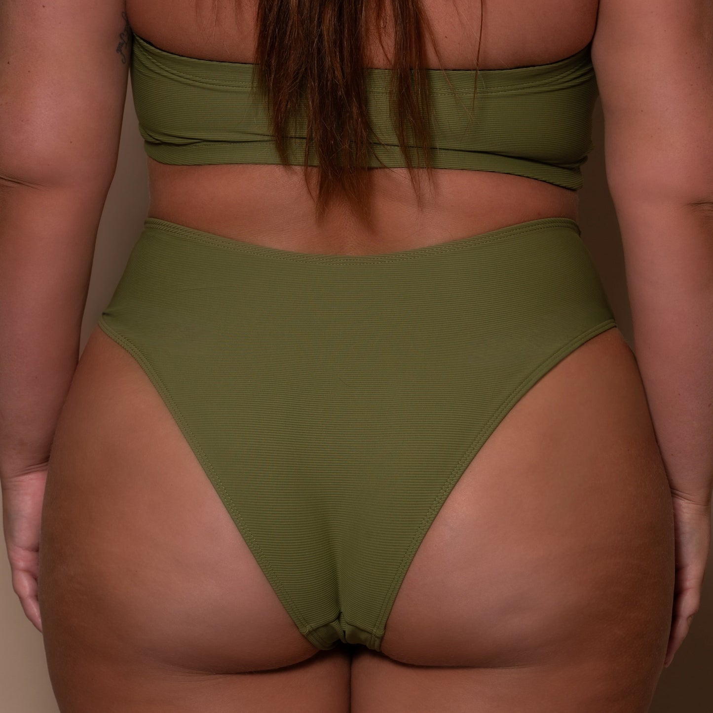 plussize woman wearing a khaki green bikini  against a beige background