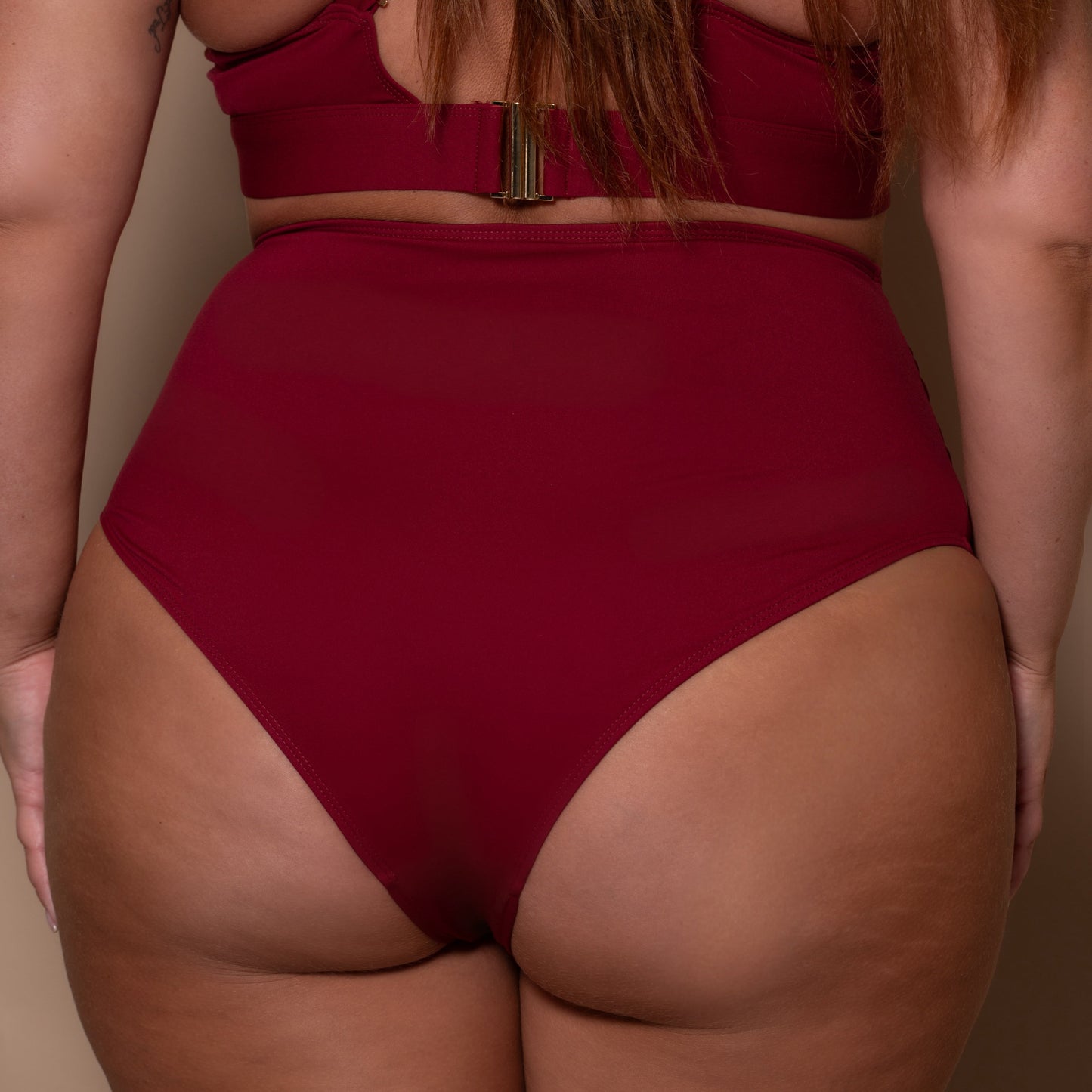 plussize woman wearing a pomegranate red bikini  against a beige background