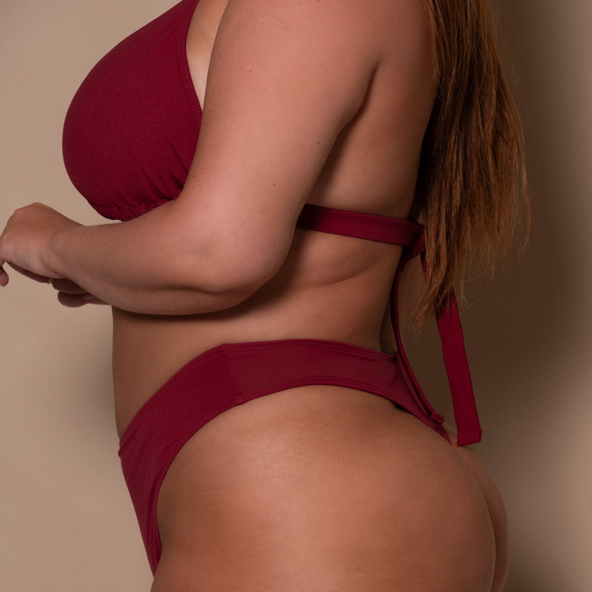 plussize woman wearing a pomegranate red bikini  against a beige background