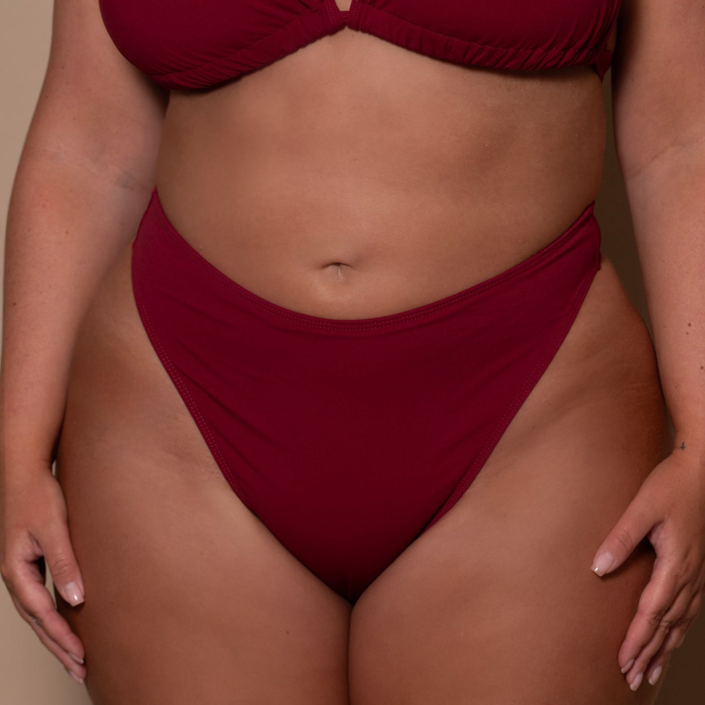 plussize woman wearing a pomegranate red bikini  against a beige background