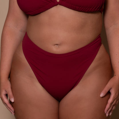 plussize woman wearing a pomegranate red bikini  against a beige background