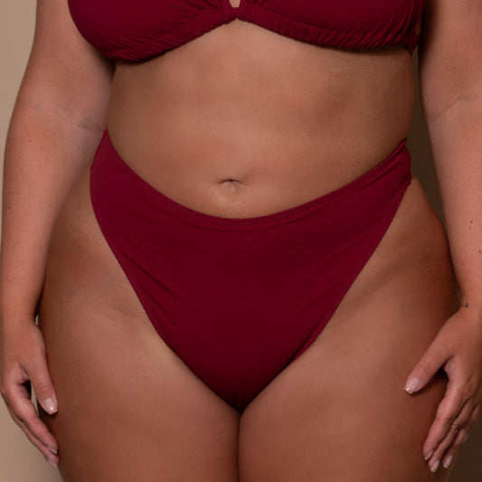plussize woman wearing a pomegranate red bikini  against a beige background