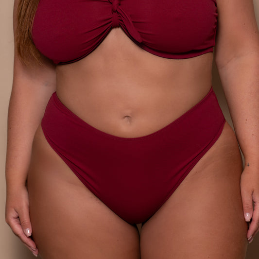 plussize woman wearing a pomegranate red bikini  against a beige background