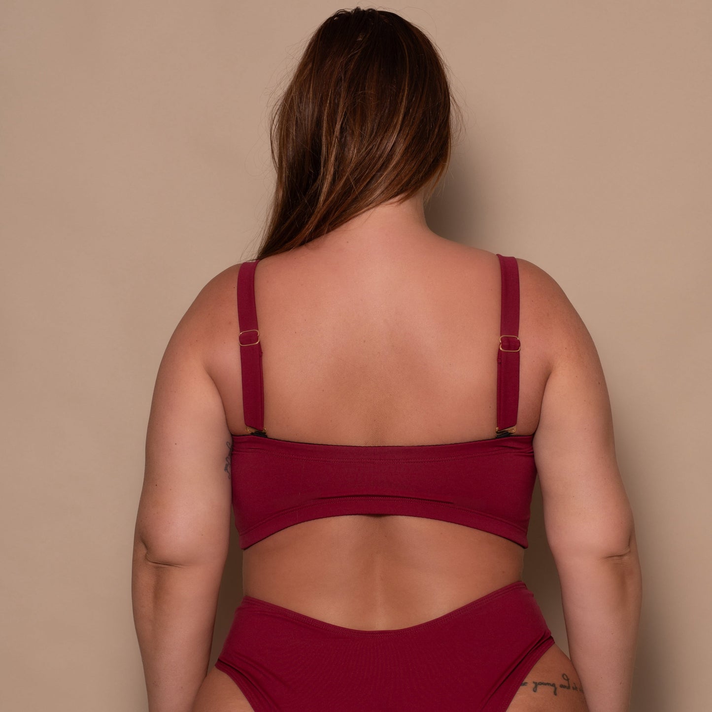 plussize woman wearing a pomegranate red bikini  against a beige background