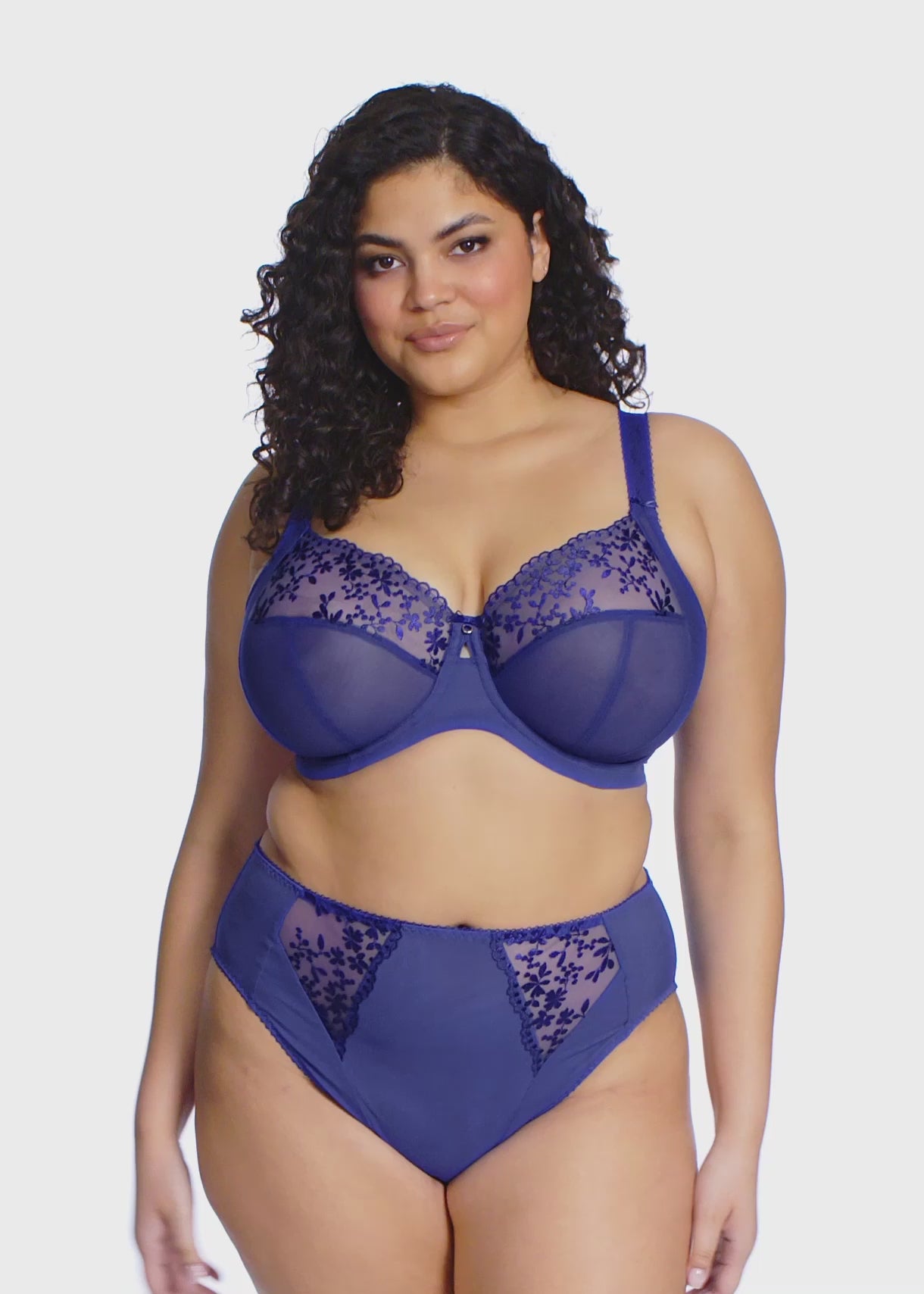 curvy woman wearing a sapphire Blue lingerie set with floral lace trim on a white background