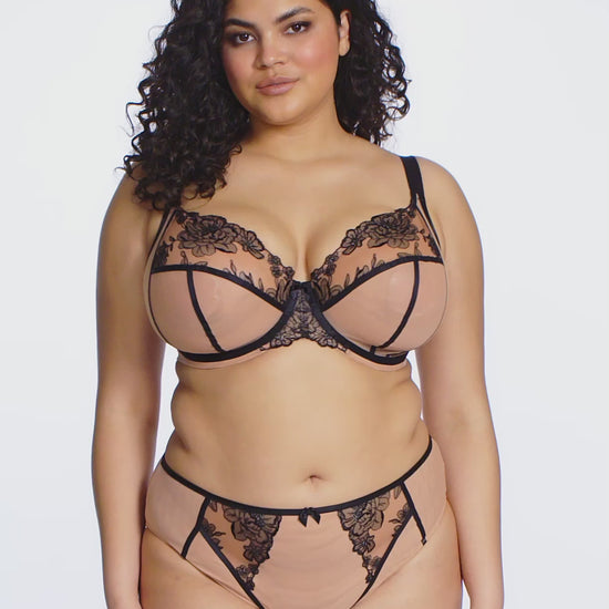 curvyoman wearing a beige lingerie set with black straps and black lace on a white background