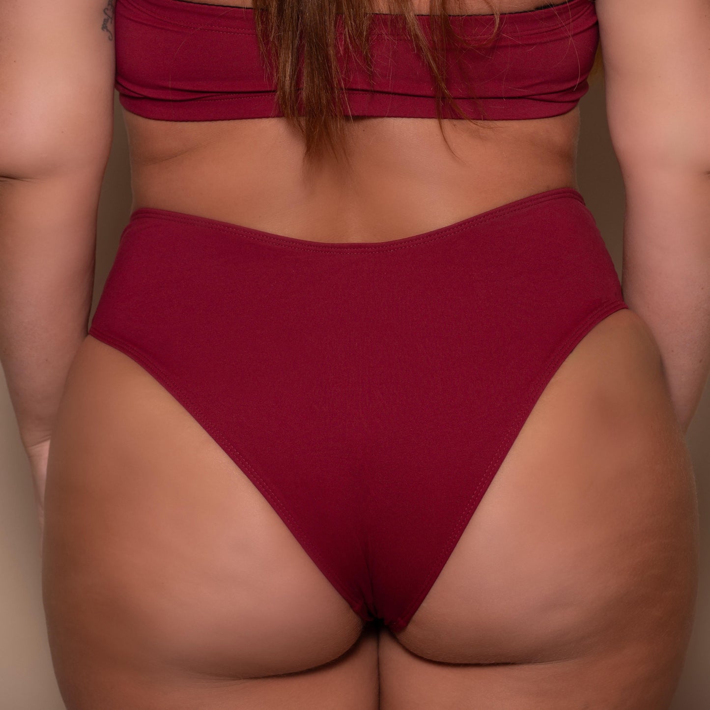 plussize woman wearing a pomegranate red bikini  against a beige background
