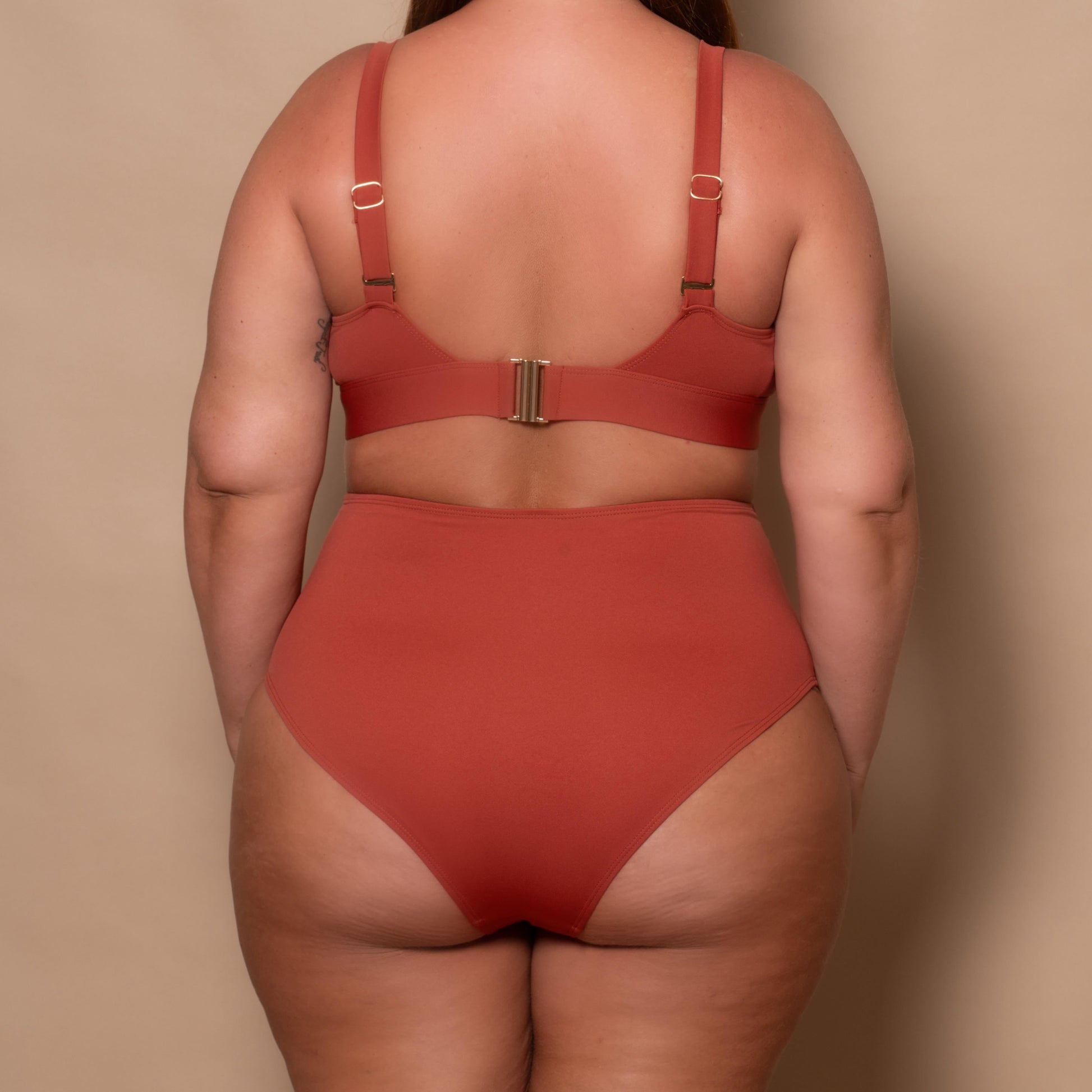 plussize woman wearing a rust red bikini set against a beige background