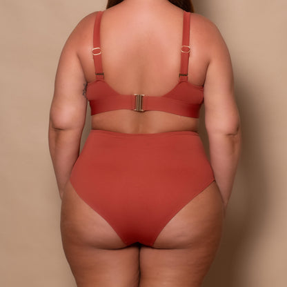 plussize woman wearing a rust red bikini set against a beige background